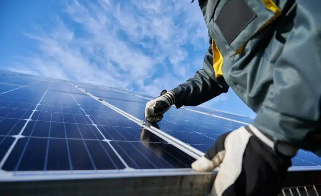 Technician installing solar panel system under blue sky with clouds